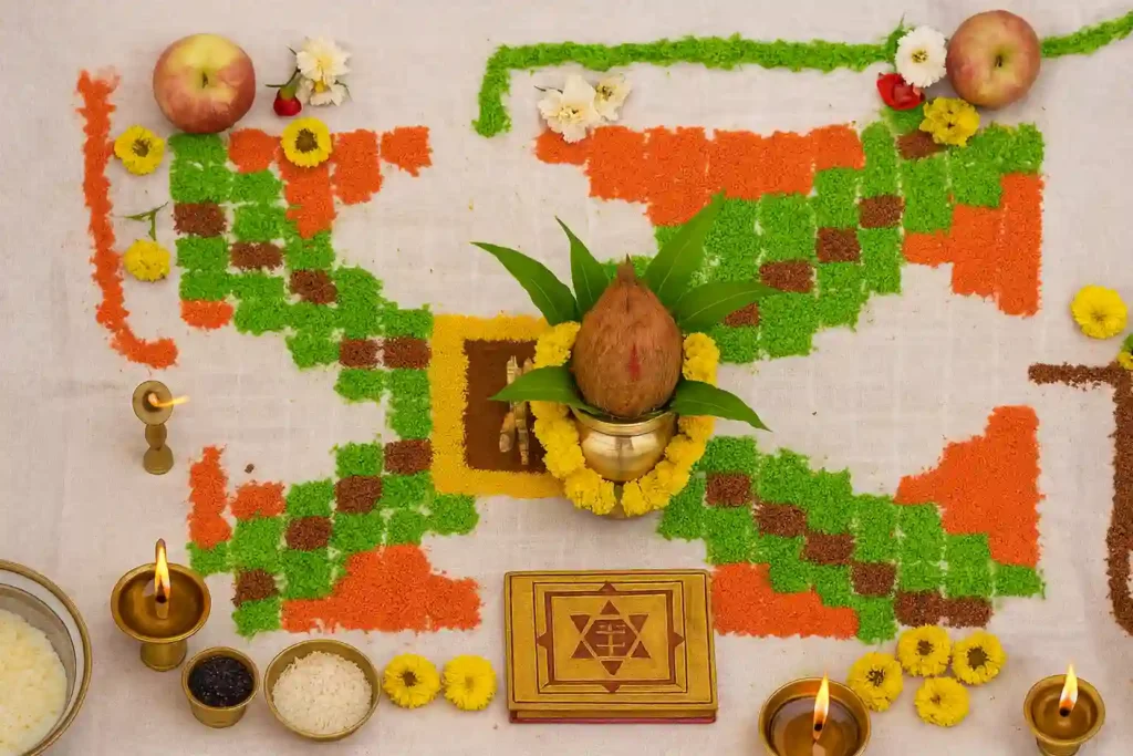 Vastu Shanti Puja arrangement showing a rangoli design made with colored powders, a decorated coconut Kalash at the center, marigold flowers, diyas, fruits, and traditional offerings